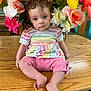 Wynter is registered to the contest to win money with this photo: baby, child, curly_hair, striped_shirt, pink_pants, flower_bouquet, artificial_flowers, wooden_table, indoor, colorful, portrait, sitting, cute, infant, smiling, face, legs, feet, furniture, decor