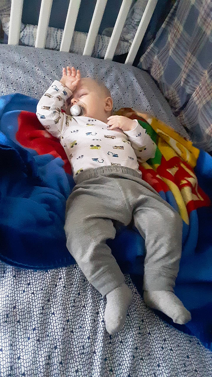 Liam is registered to the contest to win money with this photo: baby, baby_products, baby_toddler_clothing, barefoot, bedtime, child, comfort, foot, human_leg, knee, leg, linens, mammal, pattern, person, room, sitting, sleeve, sock, thigh