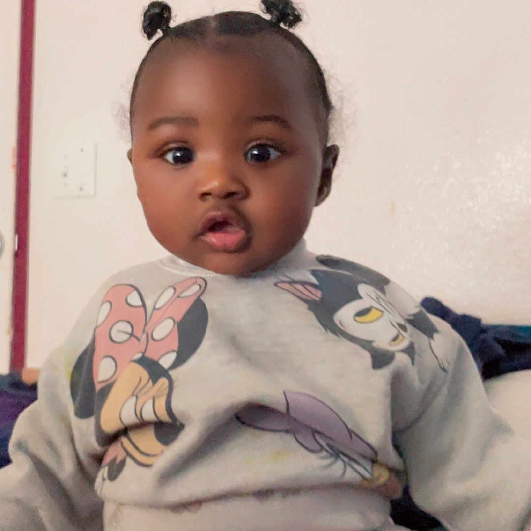 Melody is registered to the contest to win money with this photo: baby, casual, child, clothing, cute, face, hair_buns, indoor, infant, mickey_mouse, minnie_mouse, person, pink_pants, portrait, room, sitting, surprised_expression, sweatshirt, wall, young_child