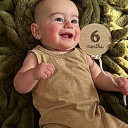 Luca joined the competition — help win amazing prizes! baby, infant, smiling, happy, child, blanket, plush, brown_clothing, wooden_sign, milestone, portrait, cute, skin, face, hand, cheeks, eyes, lying_down, indoor, celebration