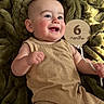 baby, infant, smiling, happy, child, blanket, plush, brown_clothing, wooden_sign, milestone, portrait, cute, skin, face, hand, cheeks, eyes, lying_down, indoor, celebration