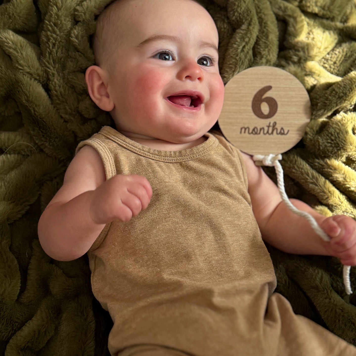 Luca joined the competition — help win amazing prizes! baby, infant, smiling, happy, child, blanket, plush, brown_clothing, wooden_sign, milestone, portrait, cute, skin, face, hand, cheeks, eyes, lying_down, indoor, celebration