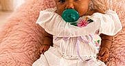 Keana is registered to the contest to win money with this photo: baby, child, infant, portrait, sitting, smiling, pacifier, headband, bow, curly_hair, dress, white_clothing, floral, pink_blanket, soft_furniture, indoor, fairy_lights, flowers, cozy, photography