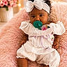 baby, child, infant, portrait, sitting, smiling, pacifier, headband, bow, curly_hair, dress, white_clothing, floral, pink_blanket, soft_furniture, indoor, fairy_lights, flowers, cozy, photography