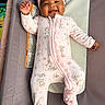 baby, infant, child, smiling, portrait, indoor, bouncer, baby_seat, pink_outfit, pajamas, headband, bow, minnie_mouse, cartoon_print, lying_down, raised_hand, happy, candid, nursery, soft_furnishings
