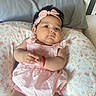 baby, infant, pink_dress, headband, bracelet, floral_cushion, cute, indoors, portrait, child, skin, face, hands, lying_down, soft_light, plush, cozy, adorable, resting, young_child