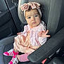 baby, child, car_seat, car_interior, seatbelt, pink_sneakers, headband, floral_bow, dress, cardigan, hand, serious_expression, infant, person, clothing, footwear, sitting, seat, interior, vehicle