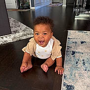 Amari is registered to the contest to win money with this photo: baby, child, crawling, floor, wooden_floor, carpet, rug, cardigan, onesie, smiling, happy, indoor, home, furniture, door, expression, person, cute, infant, playful
