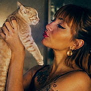 Koda a rejoint le concours — aidez-le/la à gagner de superbes lots ! woman, cat, orange_tabby, tattoo, earrings, portrait, indoor, warm_lighting, holding, pets, expression, face, animal, human, intimate_moment, closeup, hair, skin, ear, eyes