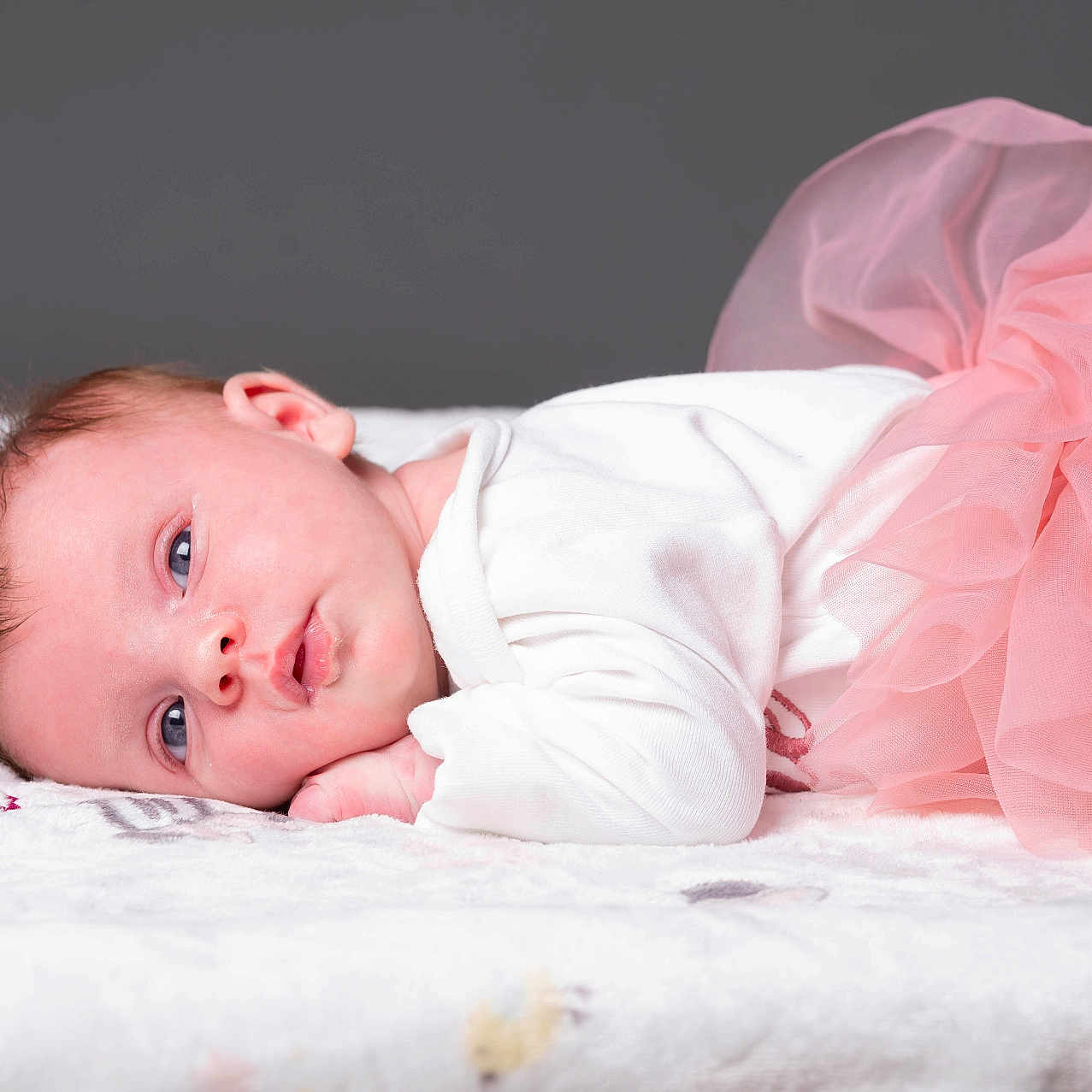 Amalya participe au concours pour gagner de l'argent avec cette photo : baby, infant, tutu, pink, white_onesie, blanket, soft_texture, lying_down, portrait, face, cute, newborn, child, blue_eyes, head, small_hands, resting, studio, soft_lighting, gray_background