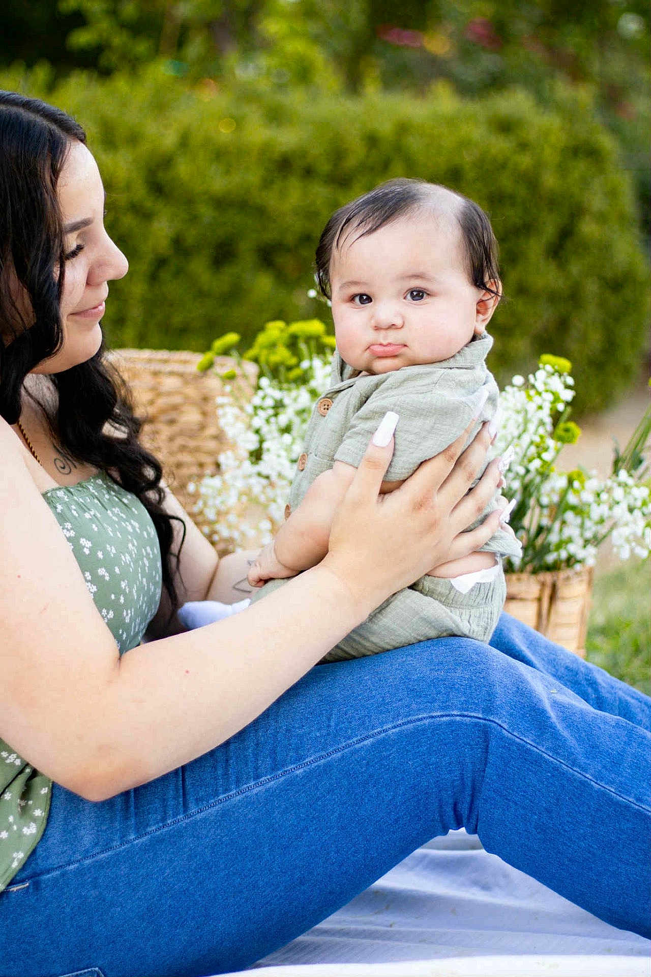 Giovanne is registered to the contest to win money with this photo: baby, woman, outdoor, greenery, flowers, holding, child, portrait, nature, casual_clothing, jeans, green_top, pouting, cute, tender, mother_and_child, garden, daylight, smile, affection