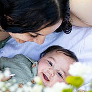 Giovanne joined the competition — help win amazing prizes! baby, adult, smile, face, flower, green_clothing, blanket, hand, hair, portrait, happy, outdoor, nature, skin, eyes, infant, parent, love, tenderness, closeup