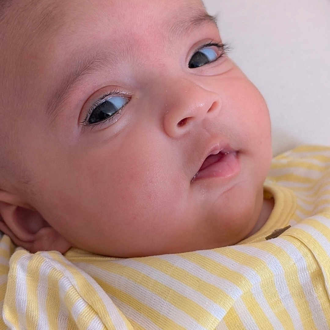 Daneen is registered to the contest to win money with this photo: baby, child, close_up, clothing, comfort, cushion, cute, expression, eyes, face, head, indoors, infant, lying_down, portrait, skin, soft_light, striped_shirt, yellow_stripes, young