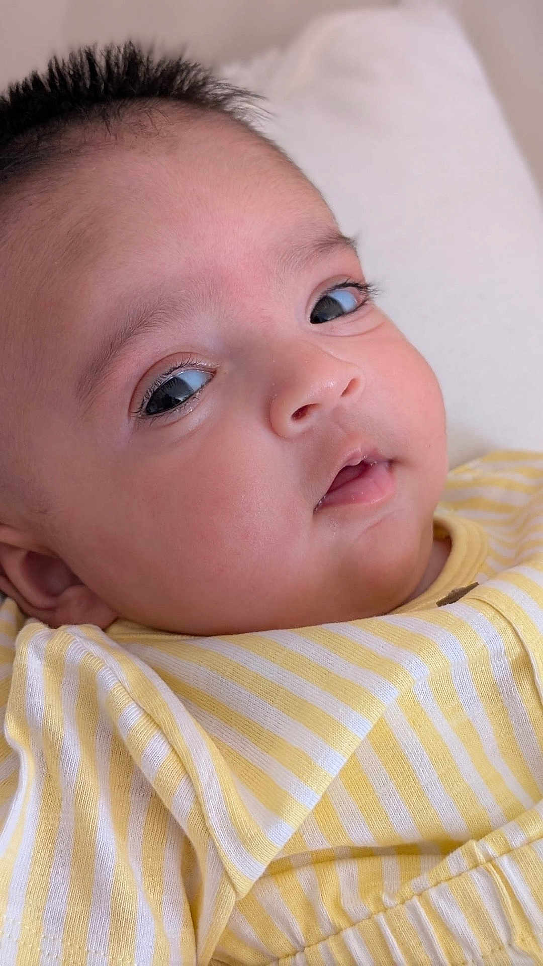 Daneen is registered to the contest to win money with this photo: baby, infant, face, eyes, skin, clothing, yellow_stripes, striped_shirt, close_up, portrait, cute, child, young, soft_light, expression, lying_down, comfort, indoors, cushion, head