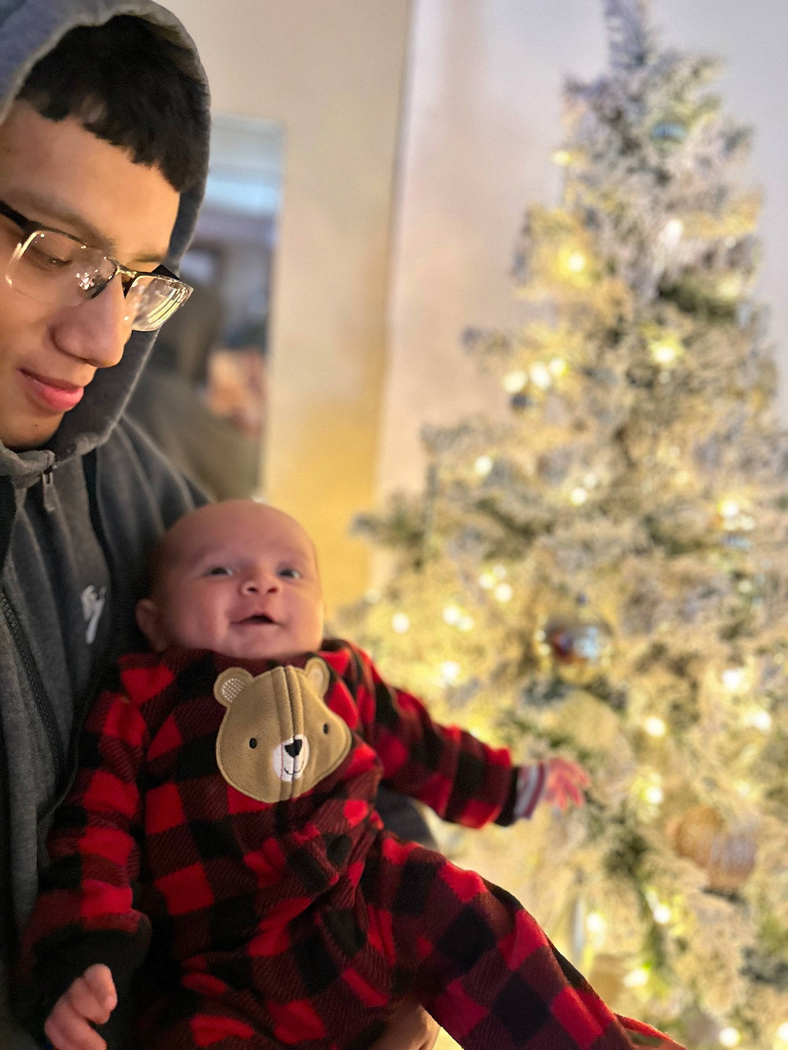 Amari is registered to the contest to win money with this photo: baby, christmas, christmas_decoration, christmas_eve, christmas_ornament, christmas_tree, event, evergreen, eyewear, glasses, happy, head, holiday_ornament, ornament, person, plaid, sleeve, standing, tartan, toddler