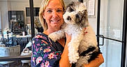 Tucker joined the competition — help win amazing prizes! woman, person, puppy, dog, pet, fluffy, white_dog, black_and_white, smiling, portrait, holding, indoor, office, glass_doors, furniture, dress, floral_sleeves, wristwatch, wood_floor, cuddling