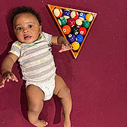 Amadeus is registered to the contest to win money with this photo: baby, child, infant, diaper, striped_shirt, billiard_balls, pool_rack, carpet, floor, indoor, playful, curious, person, skin, head, arms, legs, foot, hand, toy