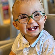 Maloë participe au concours pour gagner de l'argent avec cette photo : toddler, child, glasses, smile, happy, indoor, shirt, short_sleeve, teeth, hair, face, person, young_child, seated, cute, portrait, baby, light, background_blur, joyful