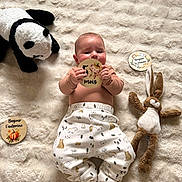 Sacha a rejoint le concours — aidez-le/la à gagner de superbes lots ! baby, infant, plush_toy, panda, bunny, blanket, card, text, clothing, socks, cute, lying_down, child, soft_texture, patterned_pants, handheld_object, indoors, portrait, smiling, young_child