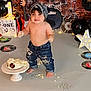 toddler, cake, birthday, messy, bandana, shirtless, jeans, music_theme, drum_set, guitar, vinyl_records, balloons, decorations, smiling, celebration, footprints, pedestal, cross_necklace, indoor, child