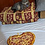 cat, tabby, pet, bed, blanket, patterned_blanket, pizza, heart_shaped_pizza, food, ham, pineapple, white_sheet, indoor, furniture, pillow, relaxed, animal, cute, cozy, gaze