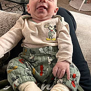 Woodson is registered to the contest to win money with this photo: baby, child, mickey_mouse, clothing, pants, socks, smile, tongue, happy, person, indoor, carpet, furniture, blanket, hand, face, cute, infant, sitting, home