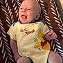 baby, infant, smiling, laughing, winnie_the_pooh, onesie, yellow_clothing, patterned_blanket, brown, white, cute, happy, child, face, skin, person, newborn, joyful, lying_down, indoors