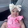 baby, child, tongue_out, white_bow, pink_outfit, car_seat, seatbelt, cute, smiling, chubby_arms, indoor, infant, clothing, headwear, person, portrait, happy, sitting, car_interior, seat