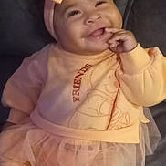 A'Zyliqua is registered to the contest to win money with this photo: baby, bow, child, couch, cozy, cute, fashion, happy, headband, indoors, infant, orange_clothing, person, playful, portrait, seated, smiling, socks, soft_lighting, tutu
