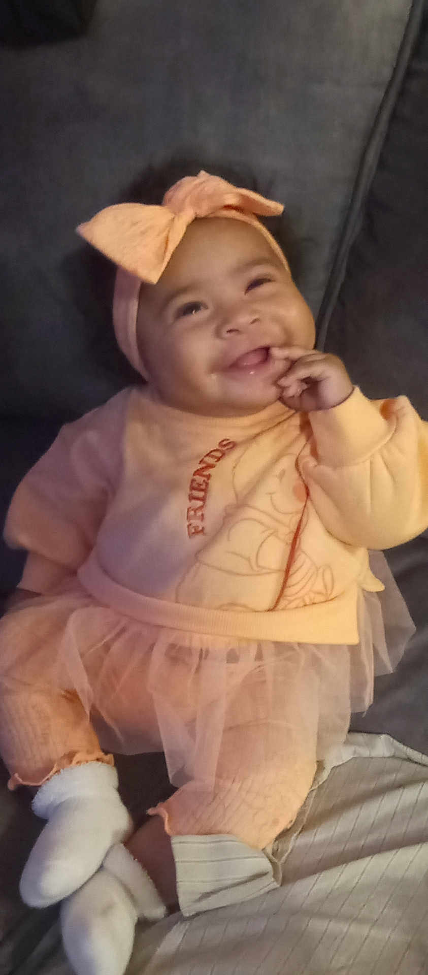 A'Zyliqua is registered to the contest to win money with this photo: baby, bow, child, couch, cozy, cute, fashion, happy, headband, indoors, infant, orange_clothing, person, playful, portrait, seated, smiling, socks, soft_lighting, tutu