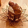 newborn, baby, sleeping, wrapped, blanket, basket, woven, wooden_floor, decorative, cozy, peaceful, indoors, soft_light, infant, resting, portrait, cute, child, warm_tones, texture