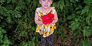 Adalynn is registered to the contest to win money with this photo: child, red_flower, hibiscus, sunflower_top, polka_dot_leggings, flip_flops, greenery, leaves, grass, outdoor, portrait, smile, blue_eyes, red_hair, hair_bun, standing, holding, nature, cute, toddler