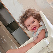 Luna is registered to the contest to win money with this photo: toddler, child, smile, curly_hair, high_chair, arm, foot, indoor, wall, doorway, furniture, messy, happy, person, skin, clothing, seat, head, face, expression