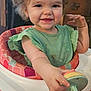Luna is registered to the contest to win money with this photo: toddler, child, baby_walker, curly_hair, green_dress, smiling, indoor, wooden_furniture, happy, cute, playful, person, furniture, toy, seat, hand, face, expression, young_child, infant