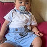 toddler, child, pacifier, suspenders, bow_tie, shorts, socks, white_shirt, couch, pillow, indoor, cute, baby, portrait, sitting, young_child, clothing, face, person, relaxed