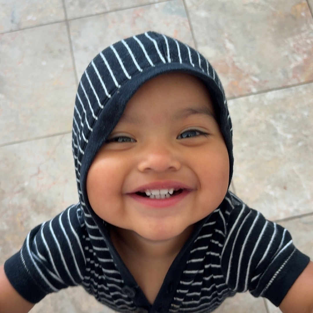 Jassiel joined the competition — help win amazing prizes! toddler, child, smile, hoodie, striped_clothing, happy, face, teeth, floor, tile, barefoot, looking_up, person, casual_clothing, cute, indoors, young_child, joyful, portrait, playful