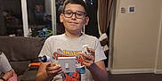 Tyler is registered to the contest to win money with this photo: child, boy, glasses, spiderman, pajamas, light_switch, plug_socket, living_room, couch, person, reflection, glass_door, curtains, tile_floor, indoor, home, smile, casual, furniture, electronics