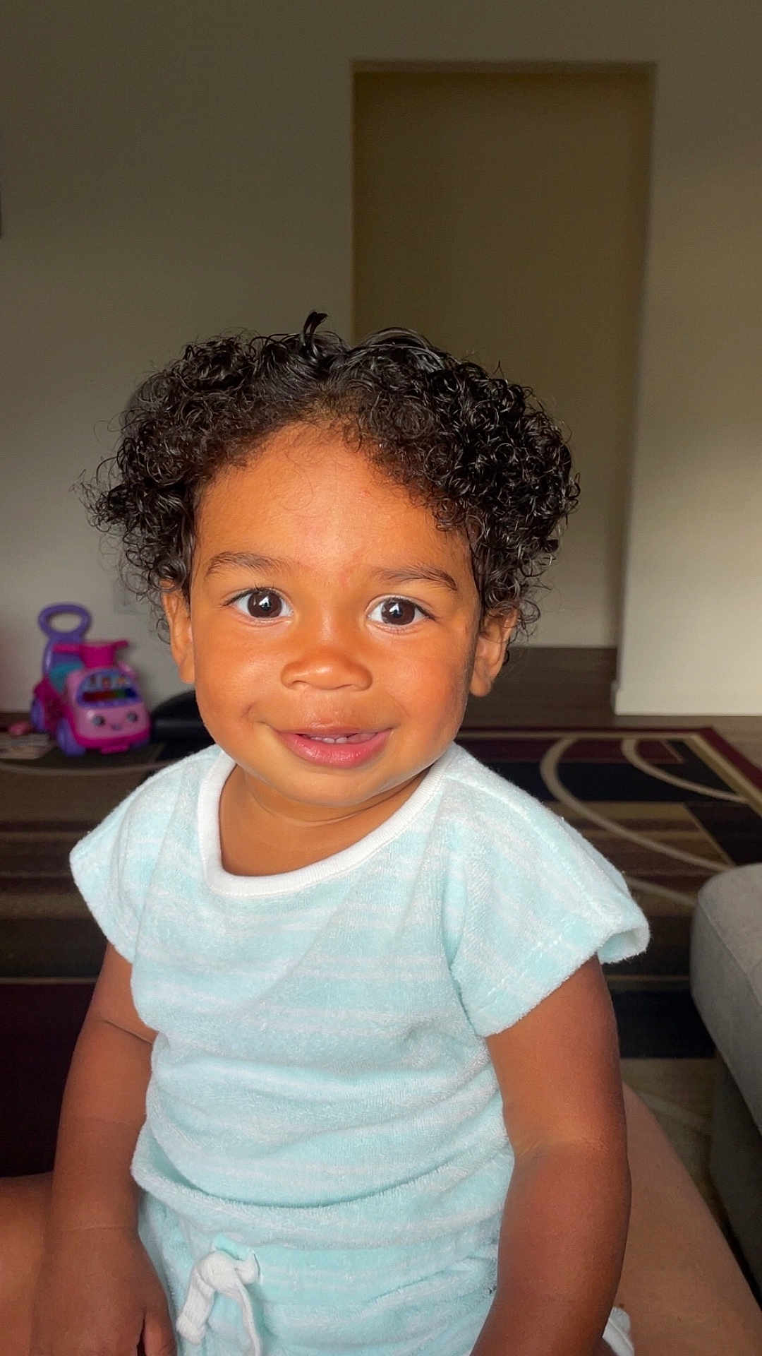 Jalin joined the competition — help win amazing prizes! toddler, child, curly_hair, smiling, indoor, toy_car, light_blue_clothing, bright_eyes, happy, portrait, person, cute, baby, young_child, sitting, home, carpet, furniture, playtime, close_up
