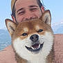 dog, shiba_inu, smiling, happy, pet, man, person, cap, outdoor, sky, mountains, water, boat, collar, fur, portrait, nature, summer, vacation, friendship