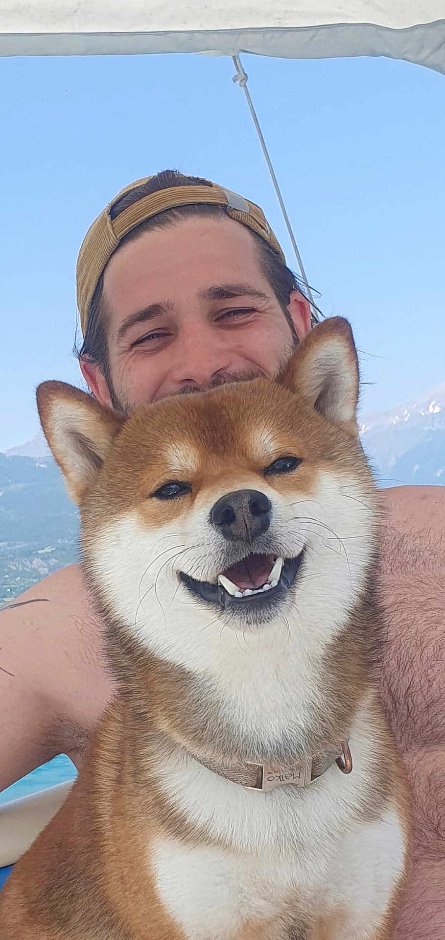 Maïko participe au concours pour gagner de l'argent avec cette photo : dog, shiba_inu, smiling, happy, pet, man, person, cap, outdoor, sky, mountains, water, boat, collar, fur, portrait, nature, summer, vacation, friendship