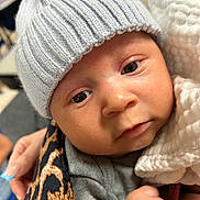 Zakai joined the competition — help win amazing prizes! baby, infant, face, hat, knit_hat, blanket, hand, closeup, cute, child, person, warm_clothing, soft_texture, wrapped, indoor, portrait, newborn, skin, expression, holding