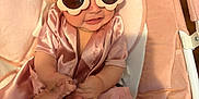 Paytom is registered to the contest to win money with this photo: baby, infant, child, sunglasses, flower_sunglasses, pink, silk_robe, baby_seat, bouncer, holding_hand, adult_hand, hair_bun, scrunched_face, smile, plush, cozy, indoor, portrait, sock, cute