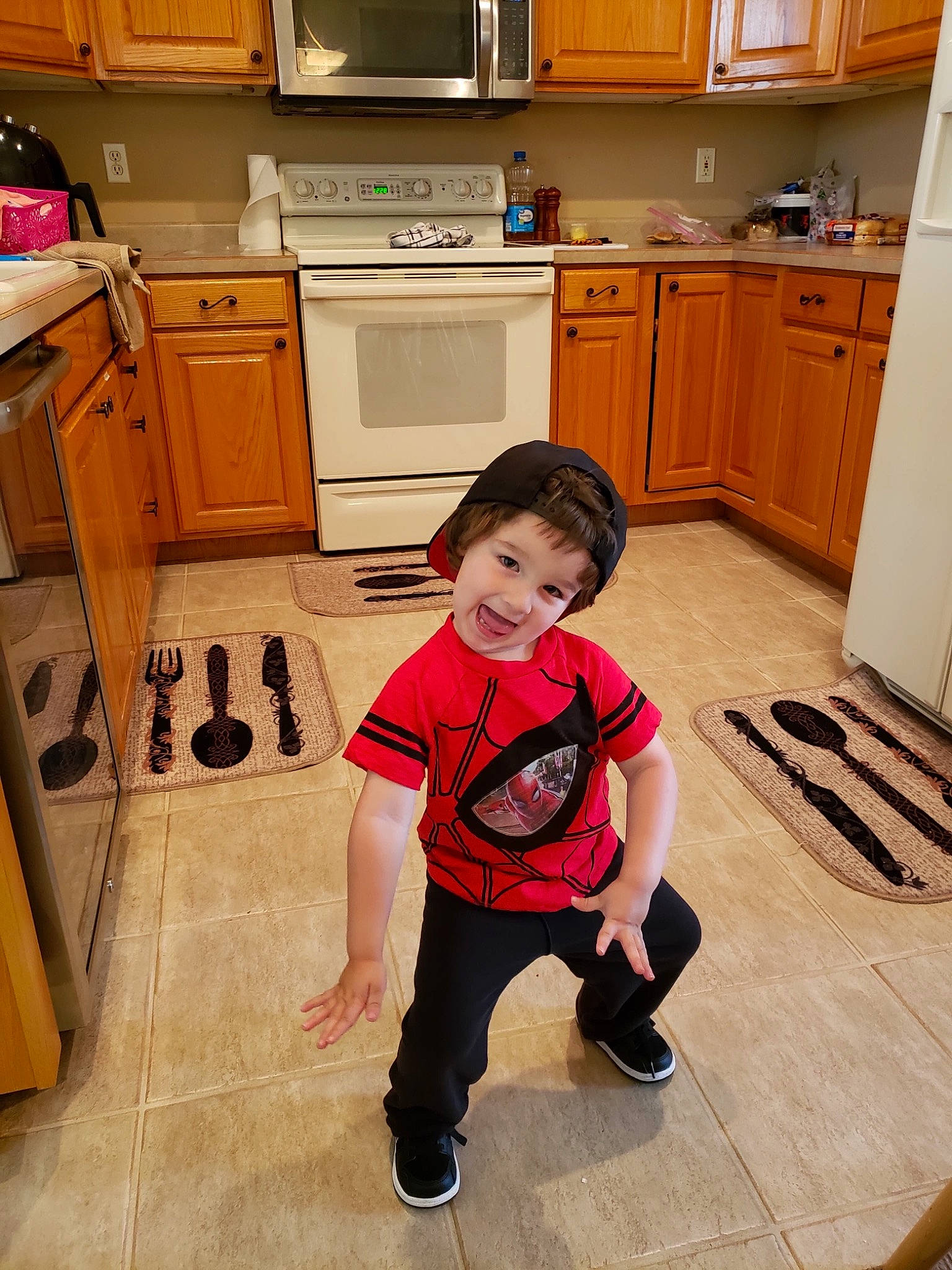 Colton is registered to the contest to win money with this photo: cabinetry, child, drawer, floor, flooring, furniture, headwear, kitchen, kitchen_appliance, leg, microwave_oven, person, play, room, standing, toddler, wood