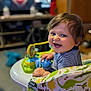 baby, smiling, walker, toy, indoor, child, dinosaur_pattern, happy, blue_eyes, striped_shirt, curly_hair, face, seat, playtime, infant, cheerful, colorful, furniture, home, closeup