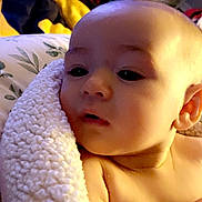 Natasha is registered to the contest to win money with this photo: baby, infant, blanket, soft_texture, close_up, face, skin, expression, curious, indoors, cozy, warm_lighting, child, person, wrapped, couch, pillow, head, ear, shoulder