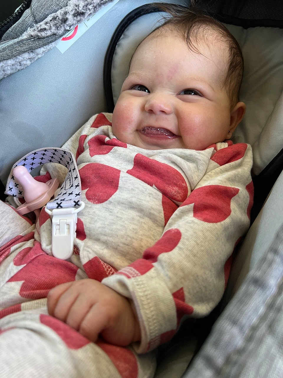 Merrilynn joined the competition — help win amazing prizes! baby, infant, smiling, car_seat, onesie, heart_pattern, pacifier, clip, hand, face, cheeks, happy, cute, child, clothing, fabric, seat, indoor, portrait, closeup