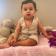 Adam a rejoint le concours — aidez-le/la à gagner de superbes lots ! toddler, child, baby, sitting, romper, beige_clothing, pink_blanket, plush_toy, bunny, indoor, curly_hair, hand_holding, purple_cloth, soft_lighting, wall, barefoot, cute, portrait, young_child, casual