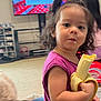 toddler, child, banana, snack, indoor, living_room, television, purple_shirt, curly_hair, person, young_child, furniture, carpet, toy, hair_tie, face, candid, real_life, casual, home