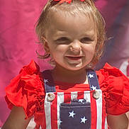 Emma joined the competition — help win amazing prizes! toddler, child, smiling, red_bow, overalls, stars, stripes, red_clothing, outdoor, portrait, happy, cute, baby, person, fashion, sunlight, face, head, background, colorful