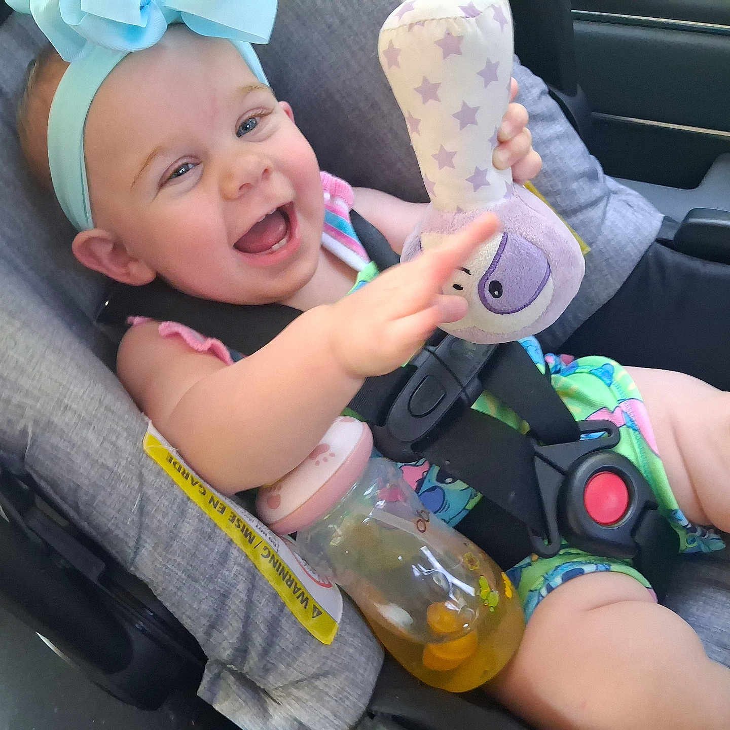 Nevah joined the competition — help win amazing prizes! baby, car_seat, child, smiling, toy, bottle, blue_bow, happy, infant, seatbelt, clothing, indoor, person, cute, playful, cheerful, small_child, car, seat, accessory